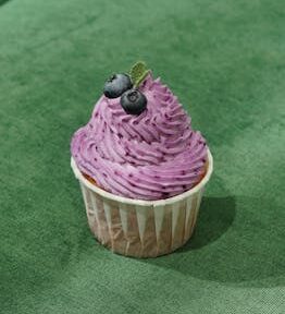 A scrumptious blueberry cupcake topped with whipped frosting and fresh blueberries.